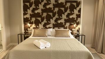 Una habitación de hotel con una cama grande, dos mesitas de noche con lámparas, un cabecero estampado con motivos de vaca y una cama bien hecha con toallas enrolladas.