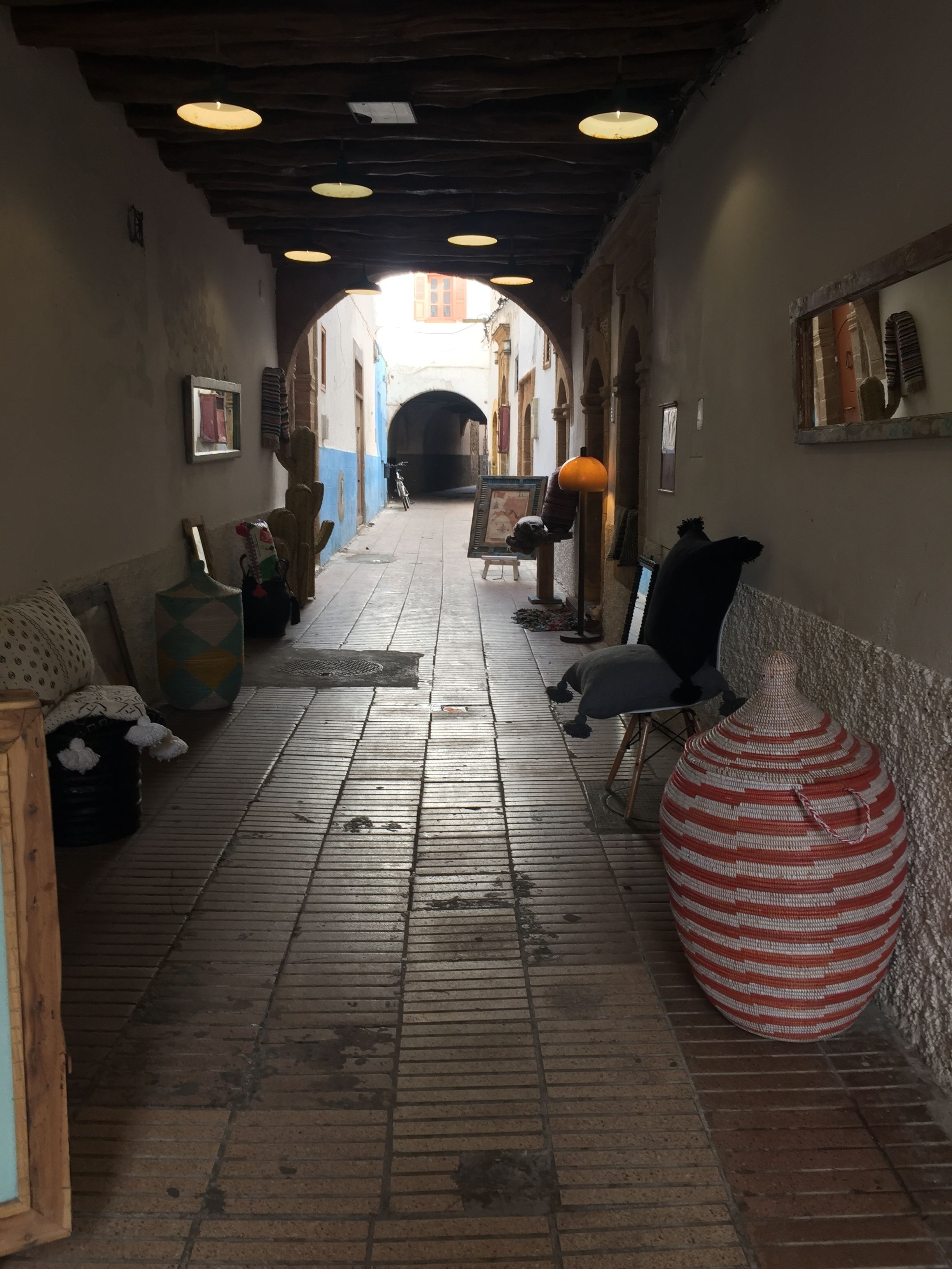 A narrow corridor with a tiled floor, wooden beams on the ceiling, and a large striped vase on the right.