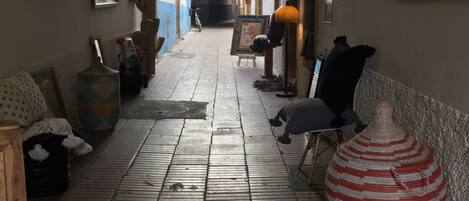 A narrow corridor with a tiled floor, wooden beams on the ceiling, and a large striped vase on the right.