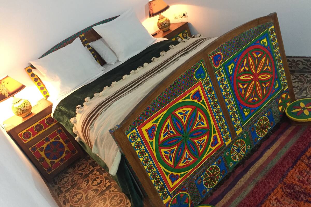 A bed with colorful geometric patterns, a white pillow, and a patterned rug.