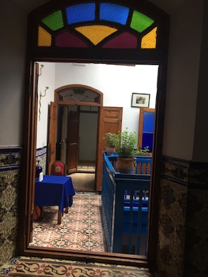 Un pasillo estrecho con suelo de baldosas, una mesa azul y una planta en maceta.