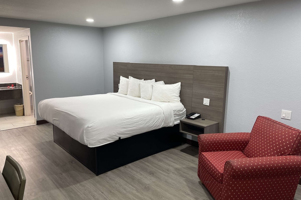 Ein Hotelzimmer mit einem großen Bett, einem Nachttisch mit Telefon, einem roten Sitzhocker mit weißen Punkten und Holzboden.