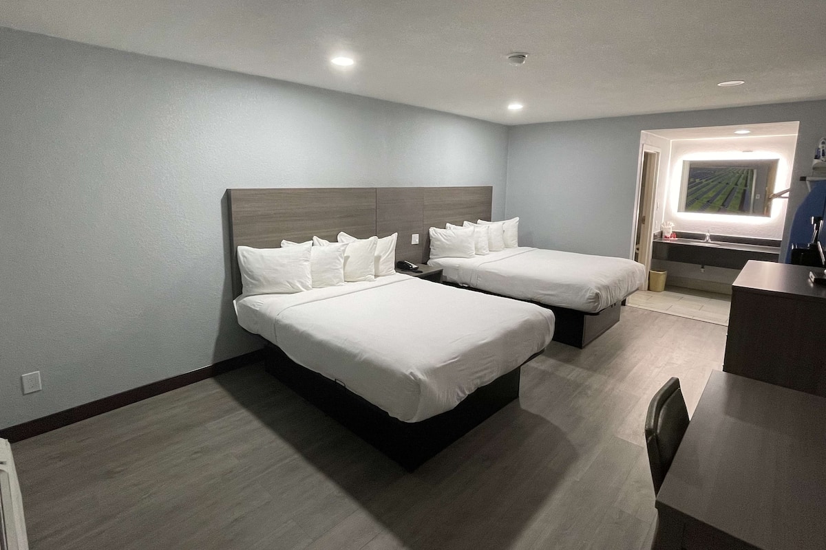Ein Hotelzimmer mit zwei Betten, einem Schreibtisch und einem Badezimmer mit Fenster.