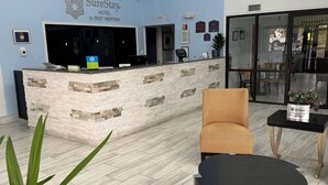 A hotel reception area with a modern design, including a reception desk, seating area, and a breakfast room visible through the glass doors. - SureStay Hotel by Best Western Childress (Childress)