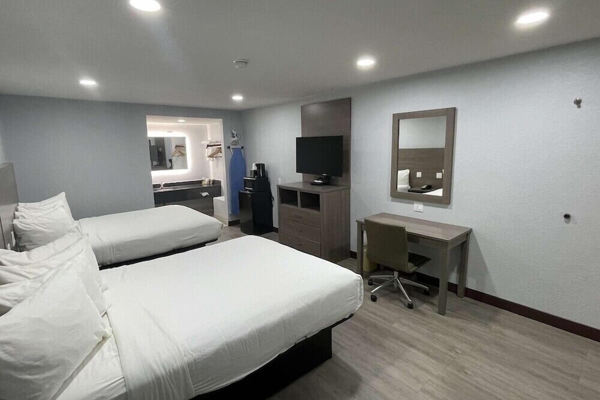 A hotel room with two beds, a desk, a TV, and a mirror.