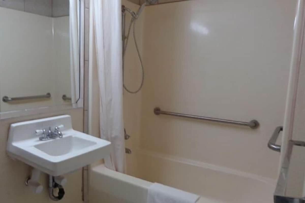 Ein Badezimmer mit Waschbecken, Spiegel, Dusche inklusive Haltegriff und Handtuchhalter.