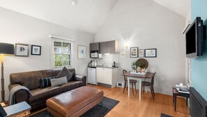 Un espace de vie compact comprenant un canapé en cuir marron, une petite kitchenette, une table à manger et un téléviseur fixé au mur.