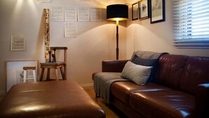 Un salon chaleureux avec un canapé en cuir marron, une chaise en bois, une lampe sur pied et une petite table.