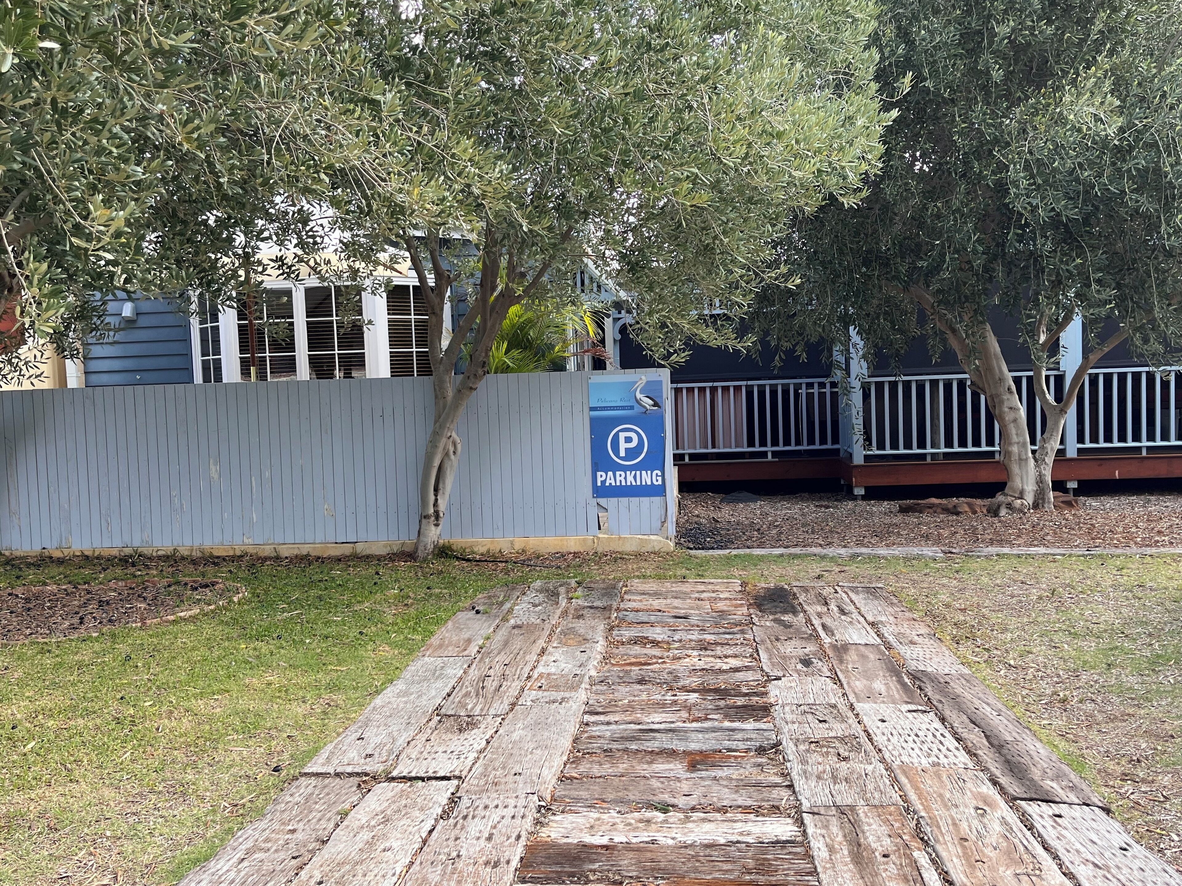 A wooden pathway leading to a parking area with a blue parking sign.