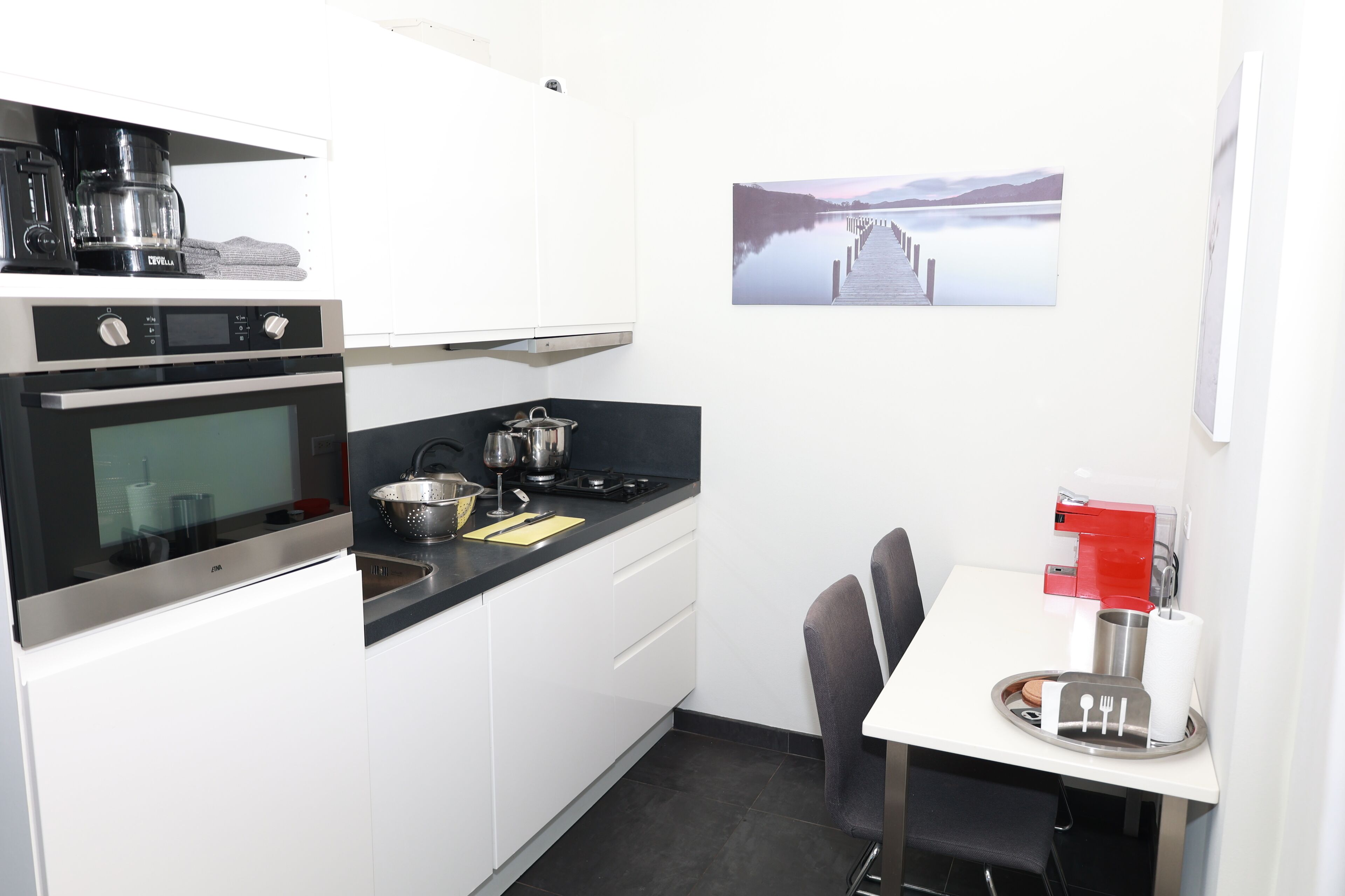 A compact kitchen with a stove, oven, and sink. There's a dining table with chairs and a red coffee machine.