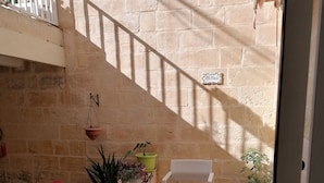 A sunlit patio with a white chair and table, potted plants, and a stone wall. - BLU HOUSE  (Sliema)