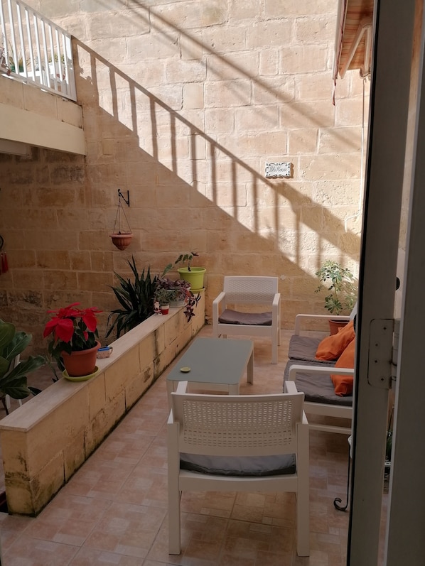 A sunlit patio with a white chair and table, potted plants, and a stone wall. - BLU HOUSE (Sliema)