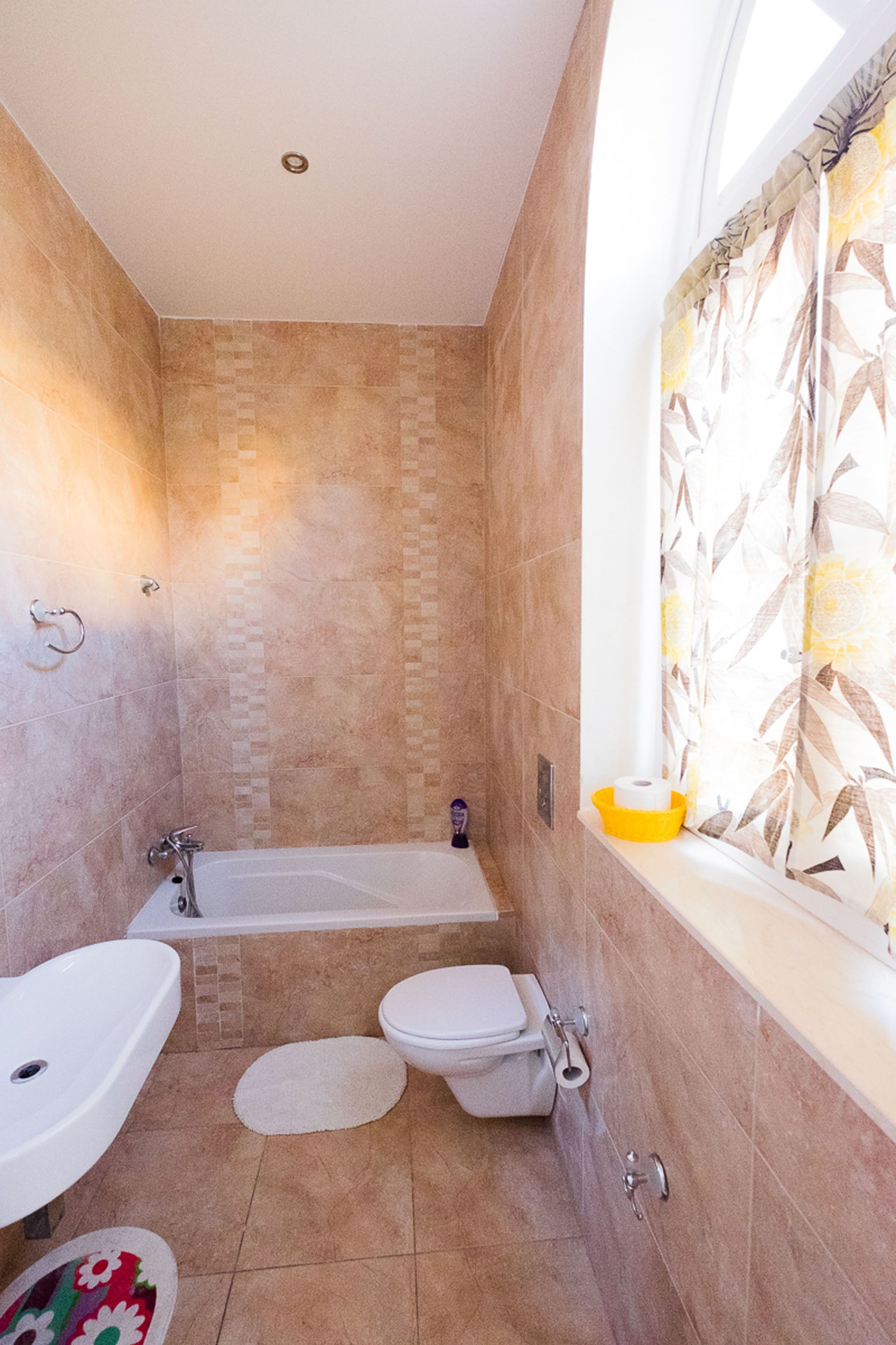 A bathroom with a bathtub, toilet, sink, and a window with floral curtains.