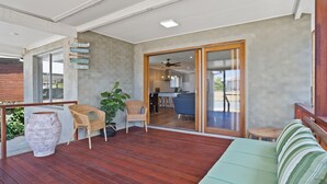 En rummelig terrasse med trægulv, fletstole, en grøn sofa og en stor plantekasse.