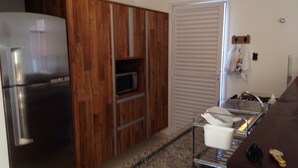 Una cocina con armarios de madera, un refrigerador de acero inoxidable, un microondas y una encimera con un lavamanos y utensilios.