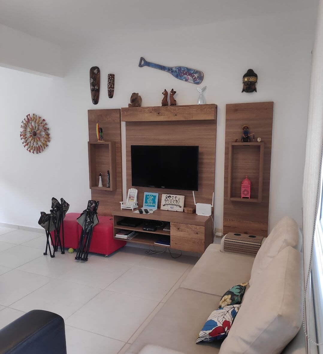 Een woonkamer met een flatscreen televisie, houten planken en een rode poef.