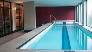 Ein Hallenbad mit klarem, blauen Wasser, einer gefliesten Liegefläche und einer roten Wand.