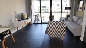 Ein modernes Wohnzimmer mit einer Couch, einem gemusterten Hocker, einem Fernseher und einem Essbereich mit Tisch und Stühlen.
