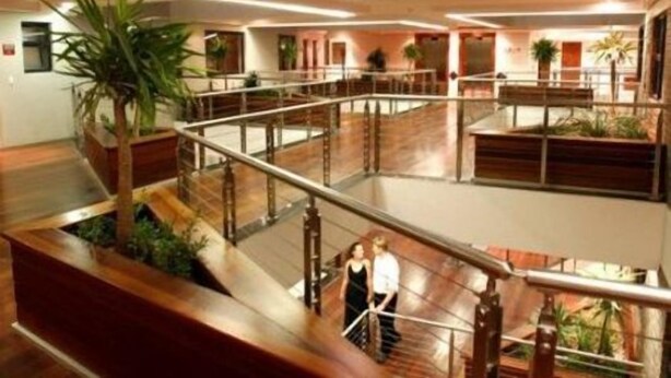 A multi-level atrium with a glass railing, wooden flooring, and potted plants.