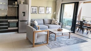 A modern living room with a sofa, coffee table, and kitchen area including a stove and refrigerator.