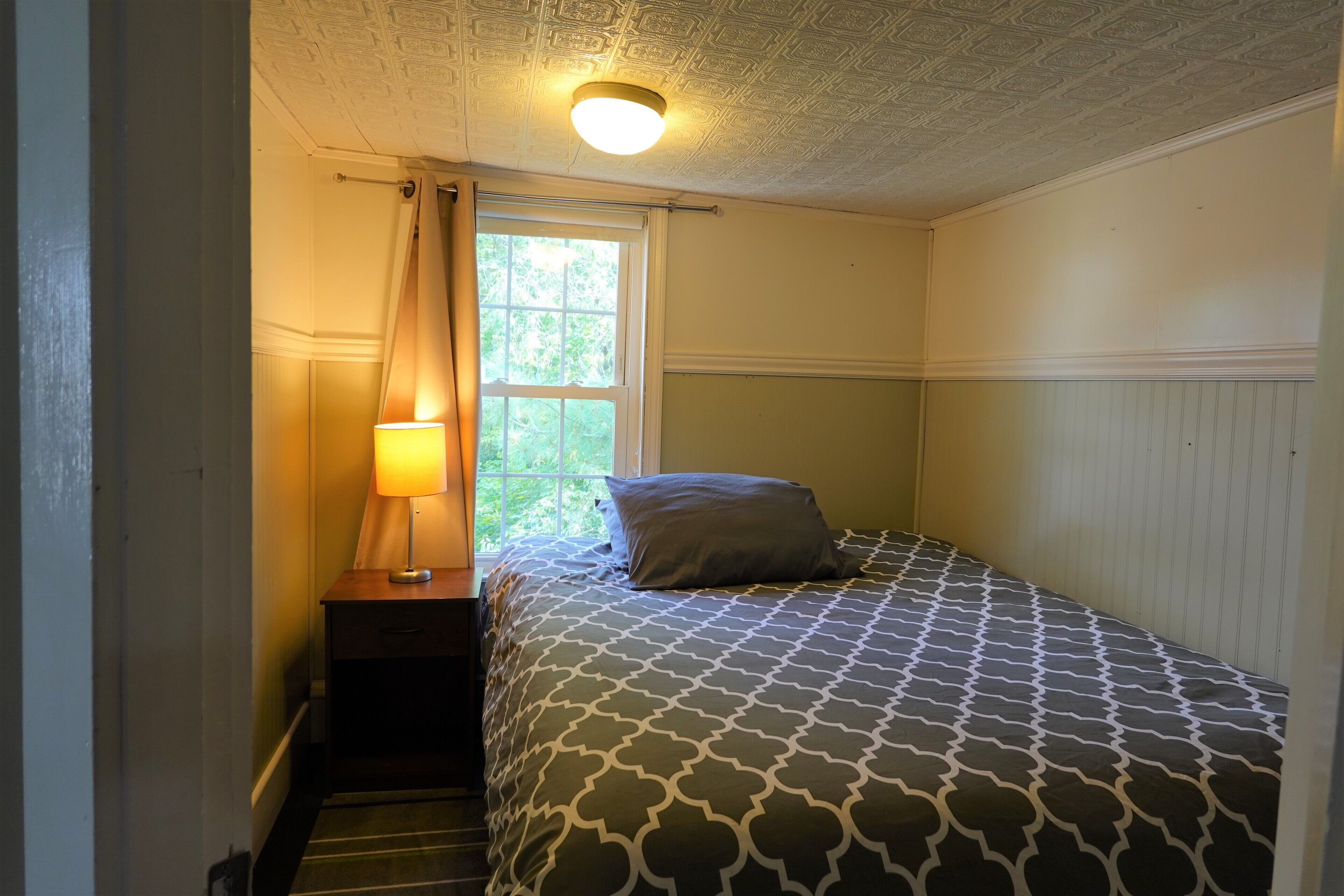 Une chambre à coucher avec une couvre-lit à motifs, une lampe de chevet et une fenêtre avec des rideaux.