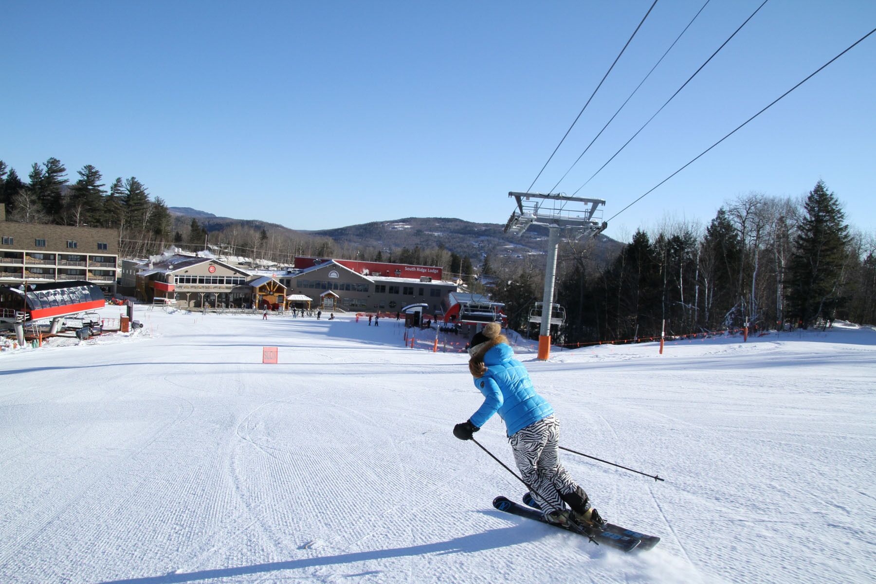A ski slope with a person skiing, buildings in the background, and a ski lift.