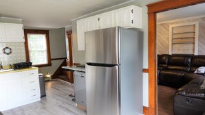 A compact kitchen with white cabinets, a stainless steel refrigerator, and a built-in dishwasher. - Sunnyside home near Sunday River, Black Mountain, Lakes, Rivers and Hikes (Rumford)