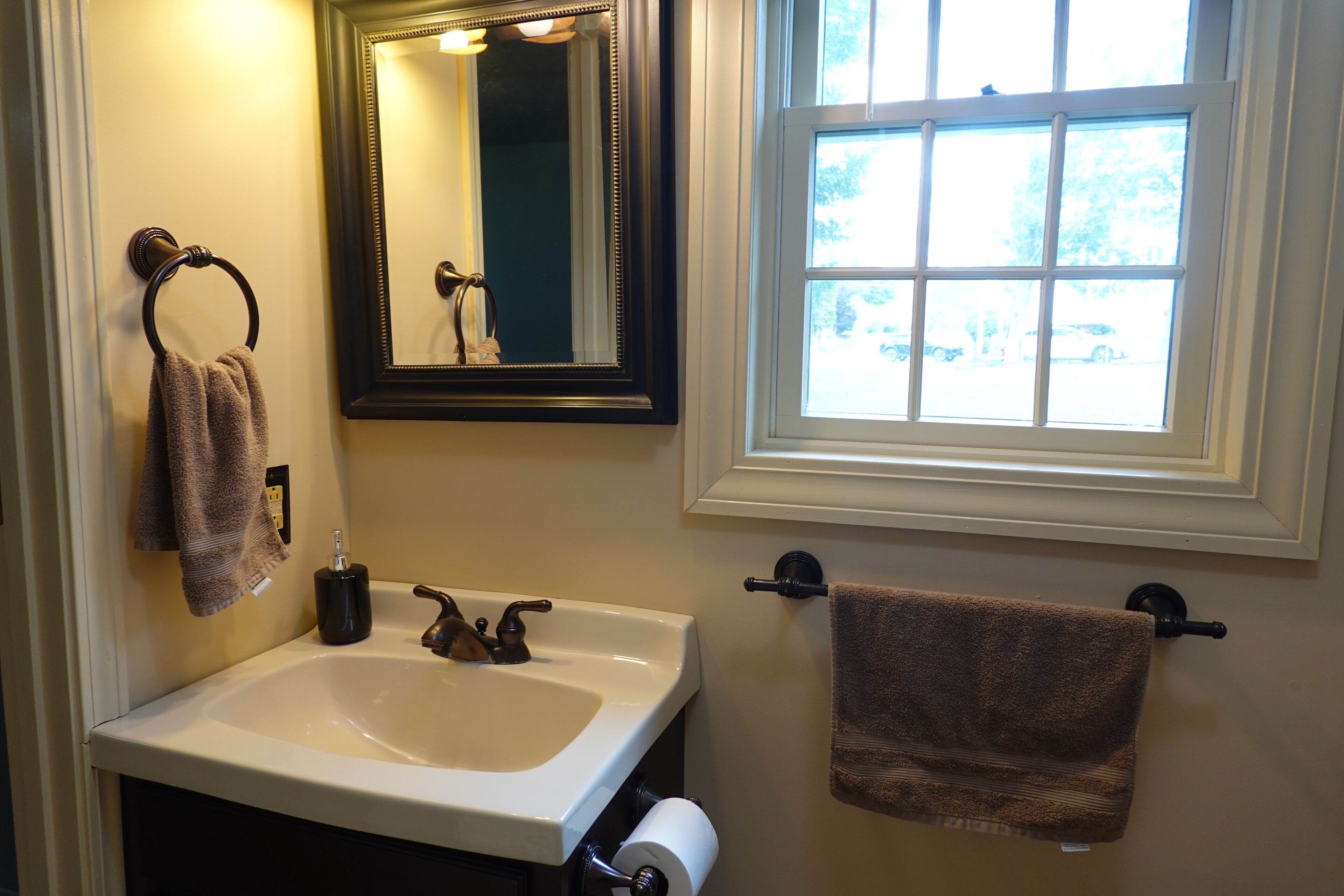 Une salle de bain équipée d’un lavabo, d’un miroir, d’un porte-serviettes et d’une fenêtre.