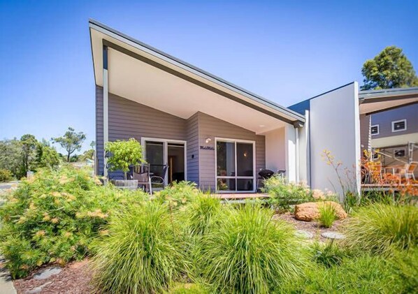 Een modern huis met een overdekte patio, omgeven door weelderig groen en een verzorgde tuin.