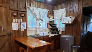 A rustic kitchen with wooden walls, a wooden bar counter, a sink, a microwave, a coffee maker, and a refrigerator. - Finca Tres Equis - Farm and Forest (Turrialba)