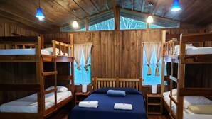A wooden cabin with bunk beds, a central bed with a blue bedspread, and a wooden table. - Finca Tres Equis - Farm and Forest (Turrialba)
