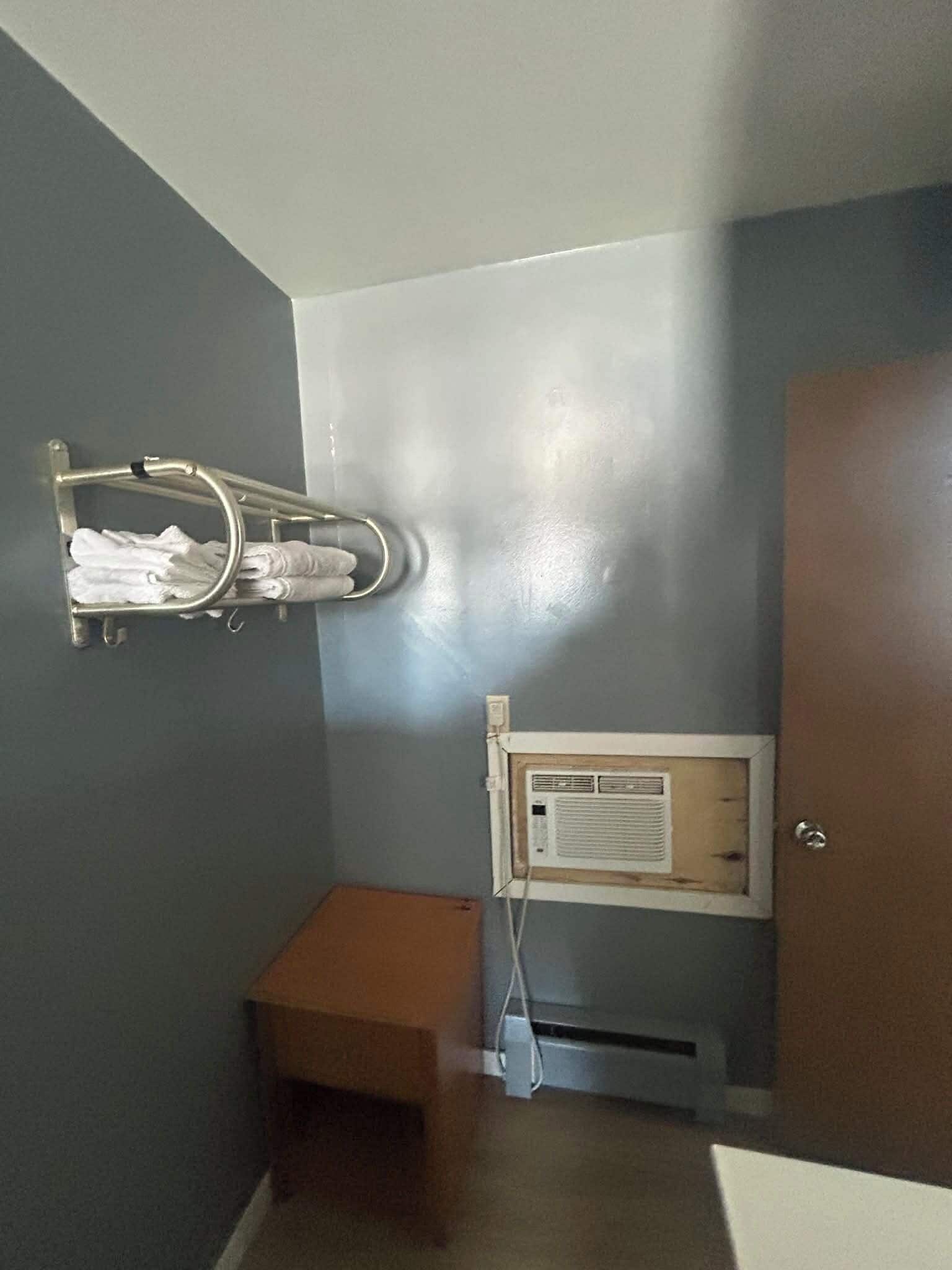 A bathroom with a towel rack, a small bench, a door, and a wall-mounted air conditioning unit.