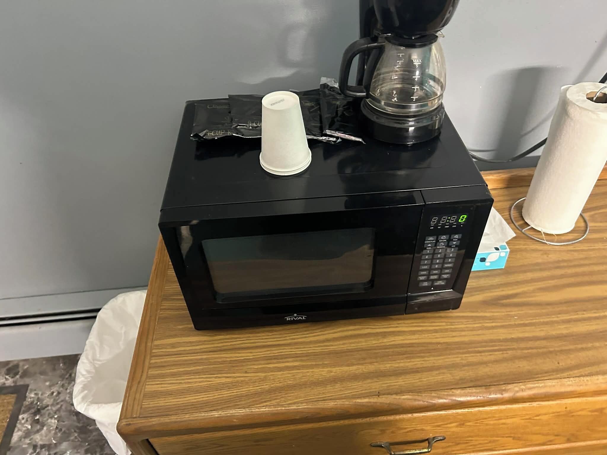 Un four à micro-ondes noir est posé sur une table en bois, à côté d’une machine à café et d’un rouleau d’essuie-tout.