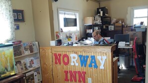 A reception desk with 'Norway Inn' signage, a computer, and a desk with various items. - Norway Inn (Jamestown)