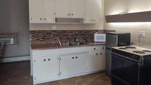 A kitchen with white cabinets, a microwave, a stove, and a tiled backsplash. - Norway Inn (Jamestown)