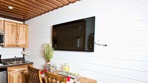 A kitchen with wooden cabinets, a wooden table with chairs, a built-in TV, and a window.