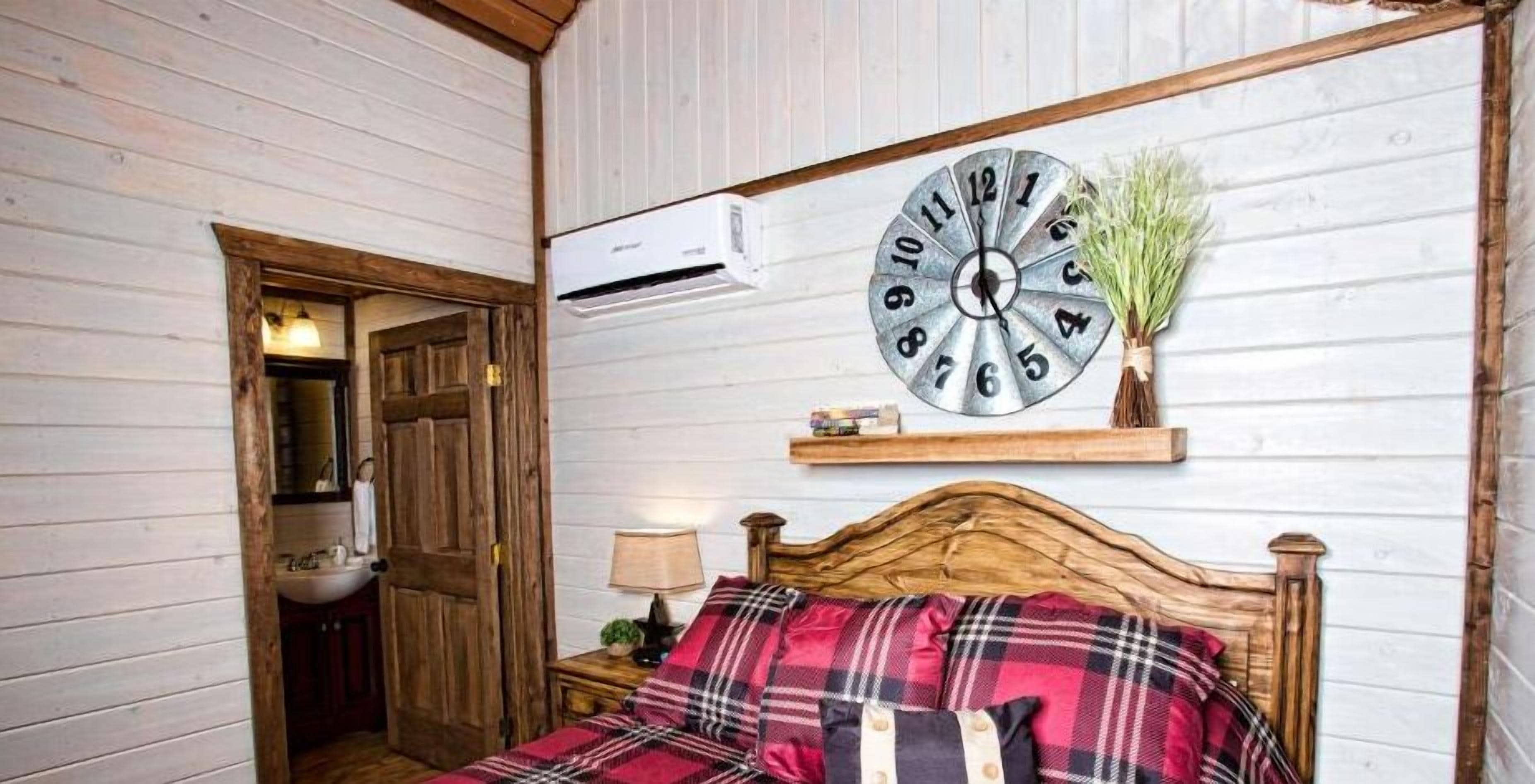 Un dormitorio con una cama de madera, un reloj de pared redondo y una pequeña estantería con una planta.