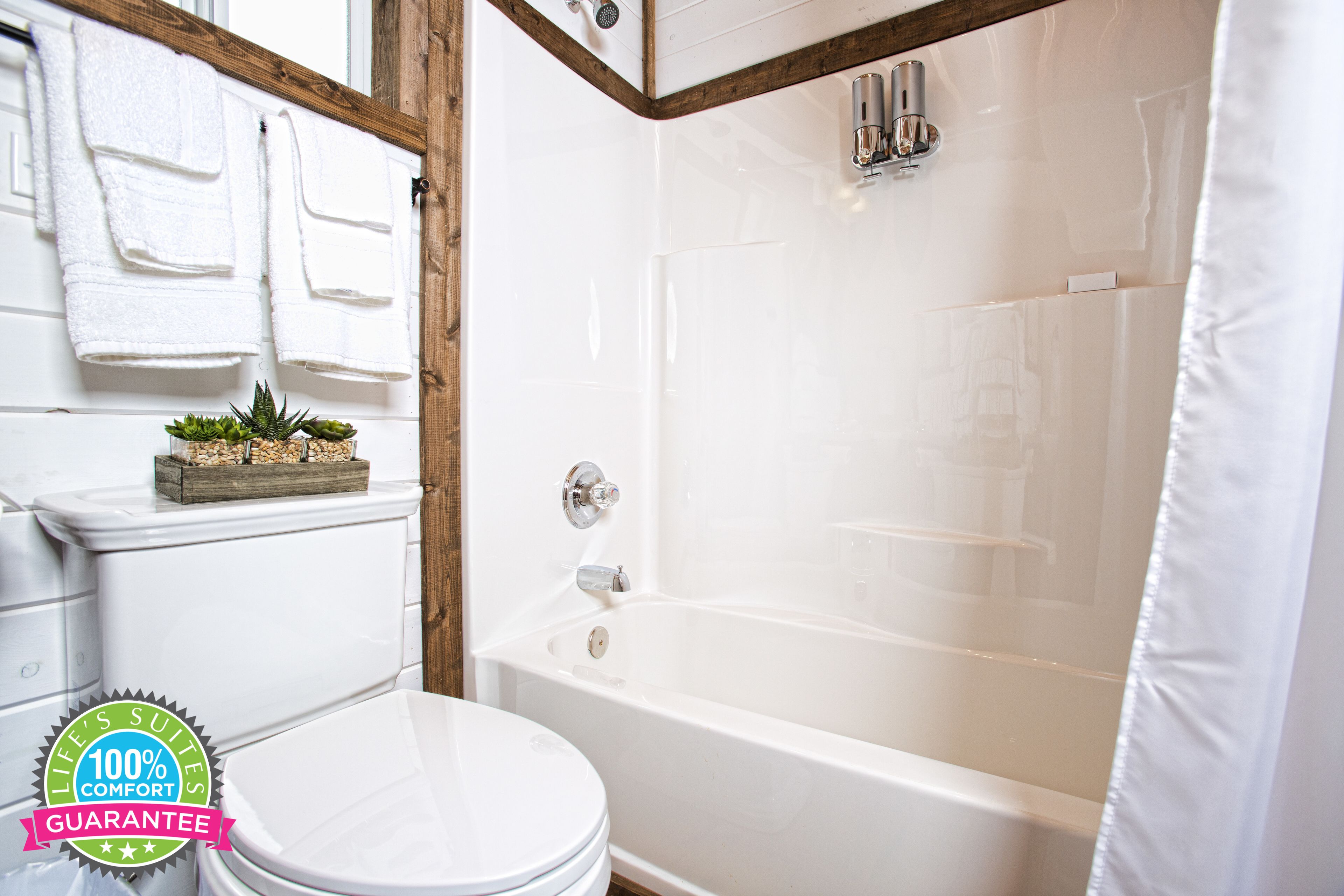 A bathroom with a white toilet, a bathtub, and a shower curtain. There are towels hanging on a rack and a small plant on the toilet.