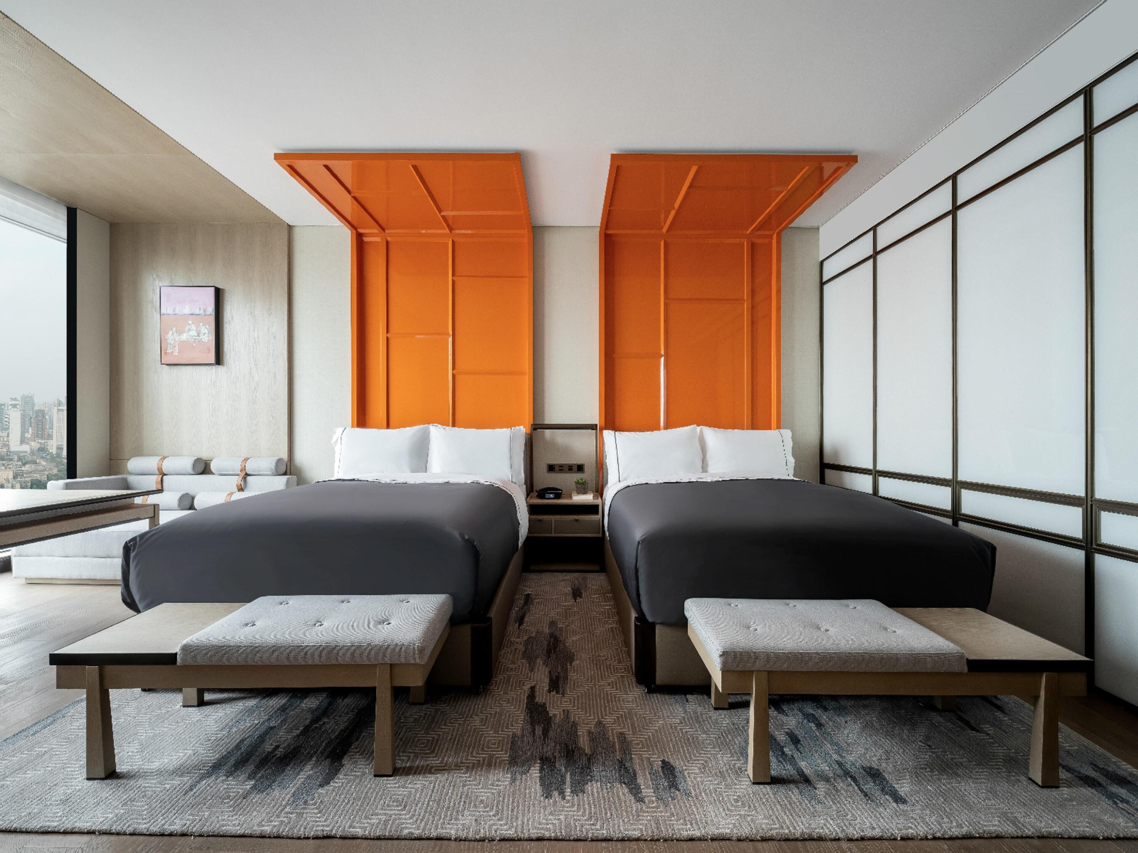 Ein Hotelzimmer mit zwei Betten, einer Sitzbank, Blick auf die Stadt und einem großen Fenster.