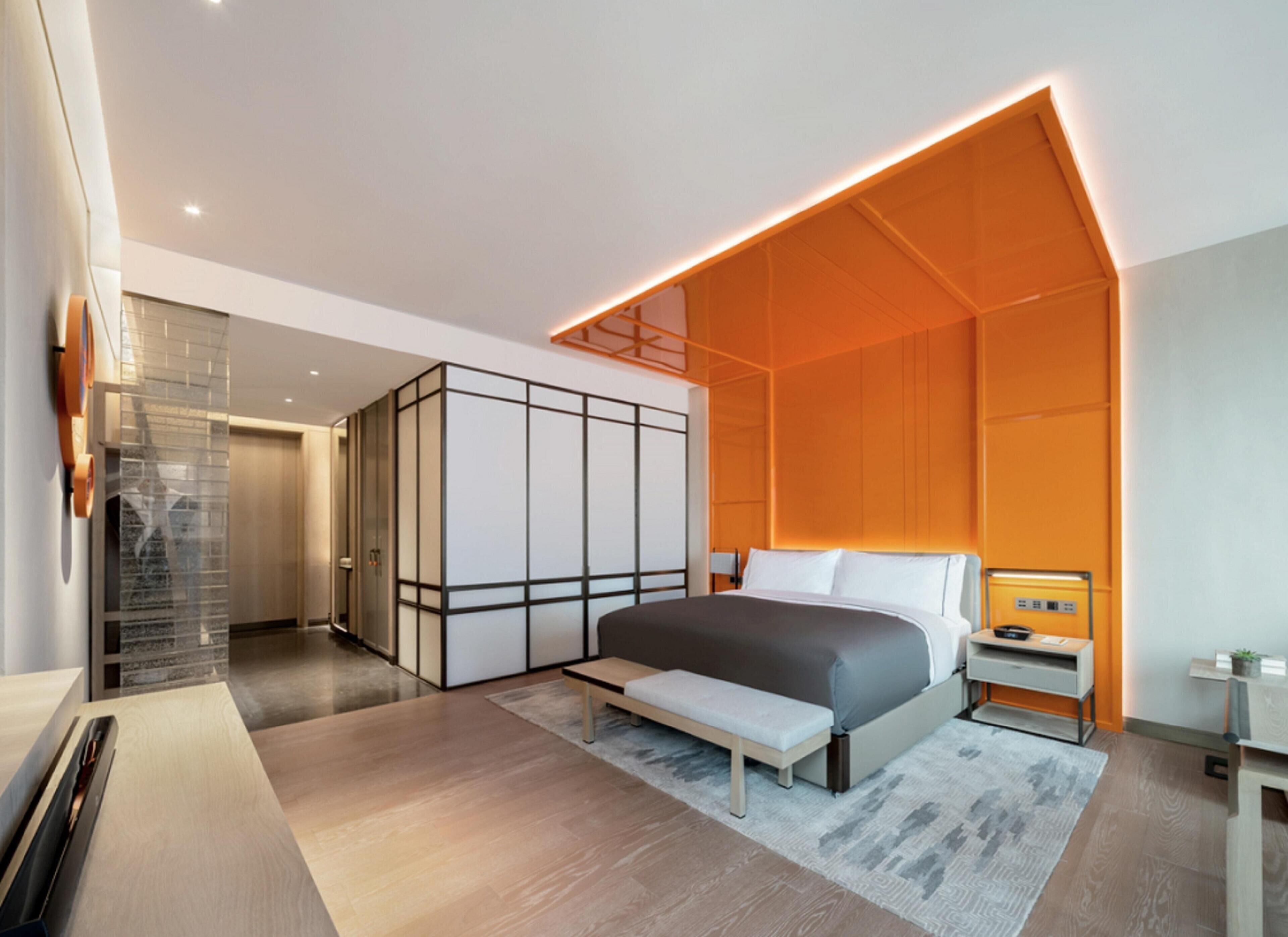 A modern bedroom with a large bed, a bench, a wardrobe, and a bedside table.