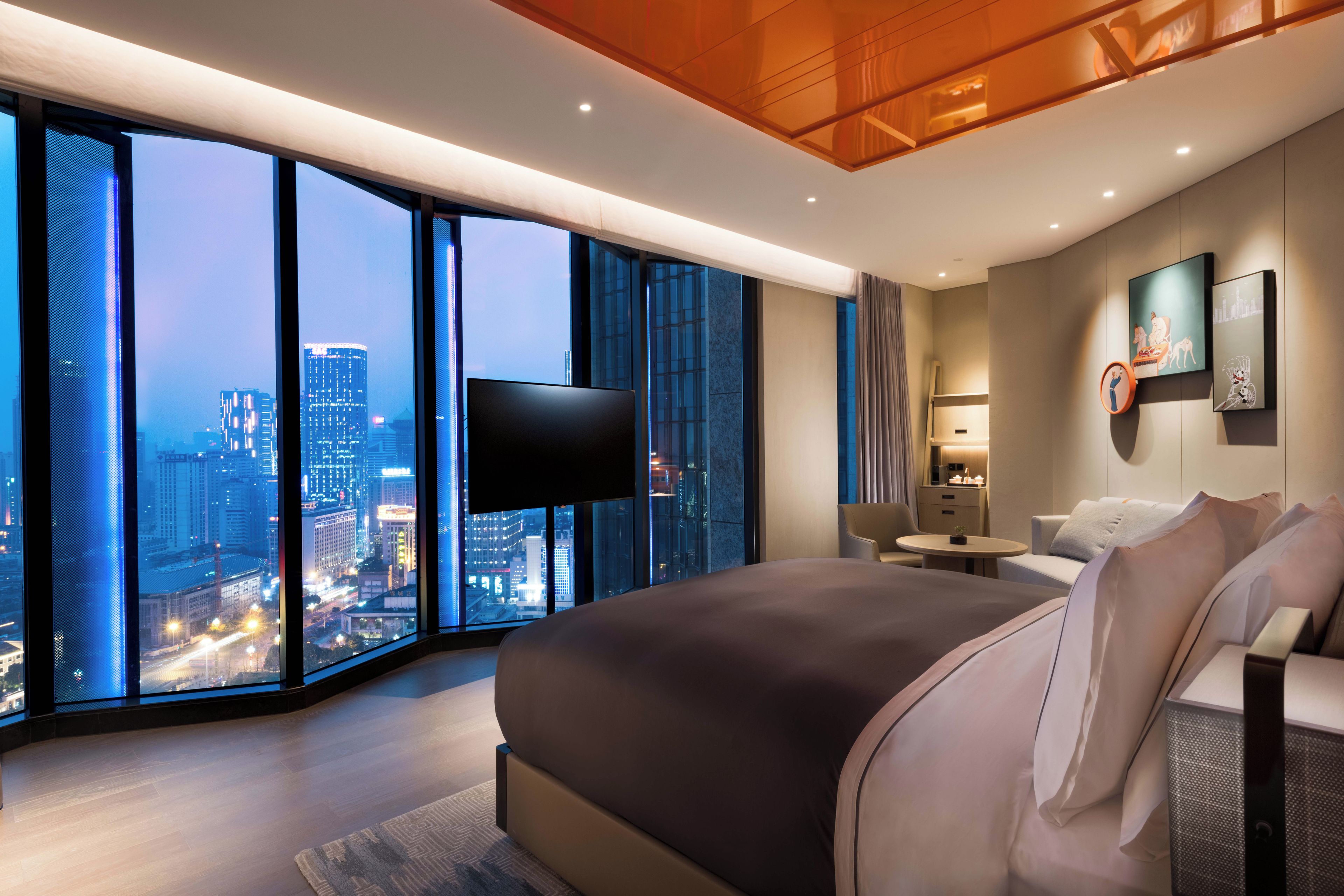 Ein modernes Hotelzimmer mit einem großen Bett, einem Flachbildfernseher, einer Couch und Blick auf die Stadt.