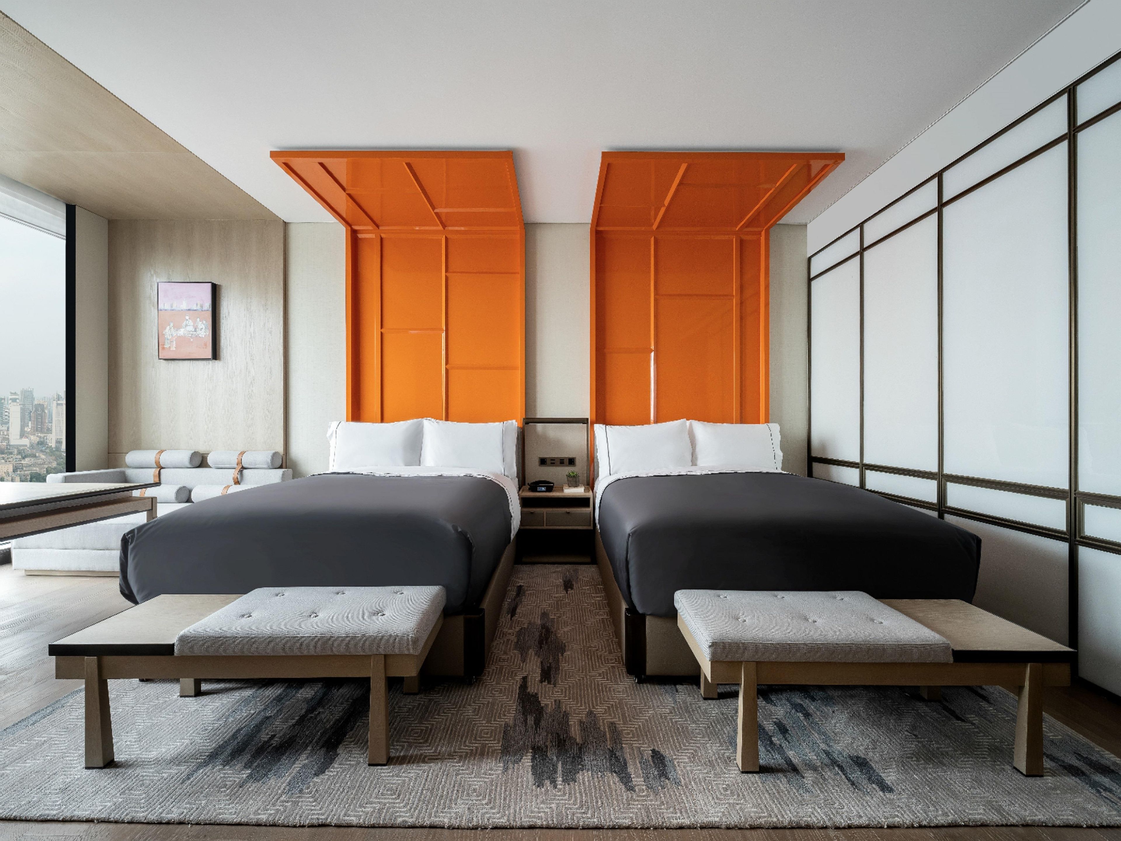 Une chambre d’hôtel avec deux lits, un banc, une vue sur la ville et une grande fenêtre.