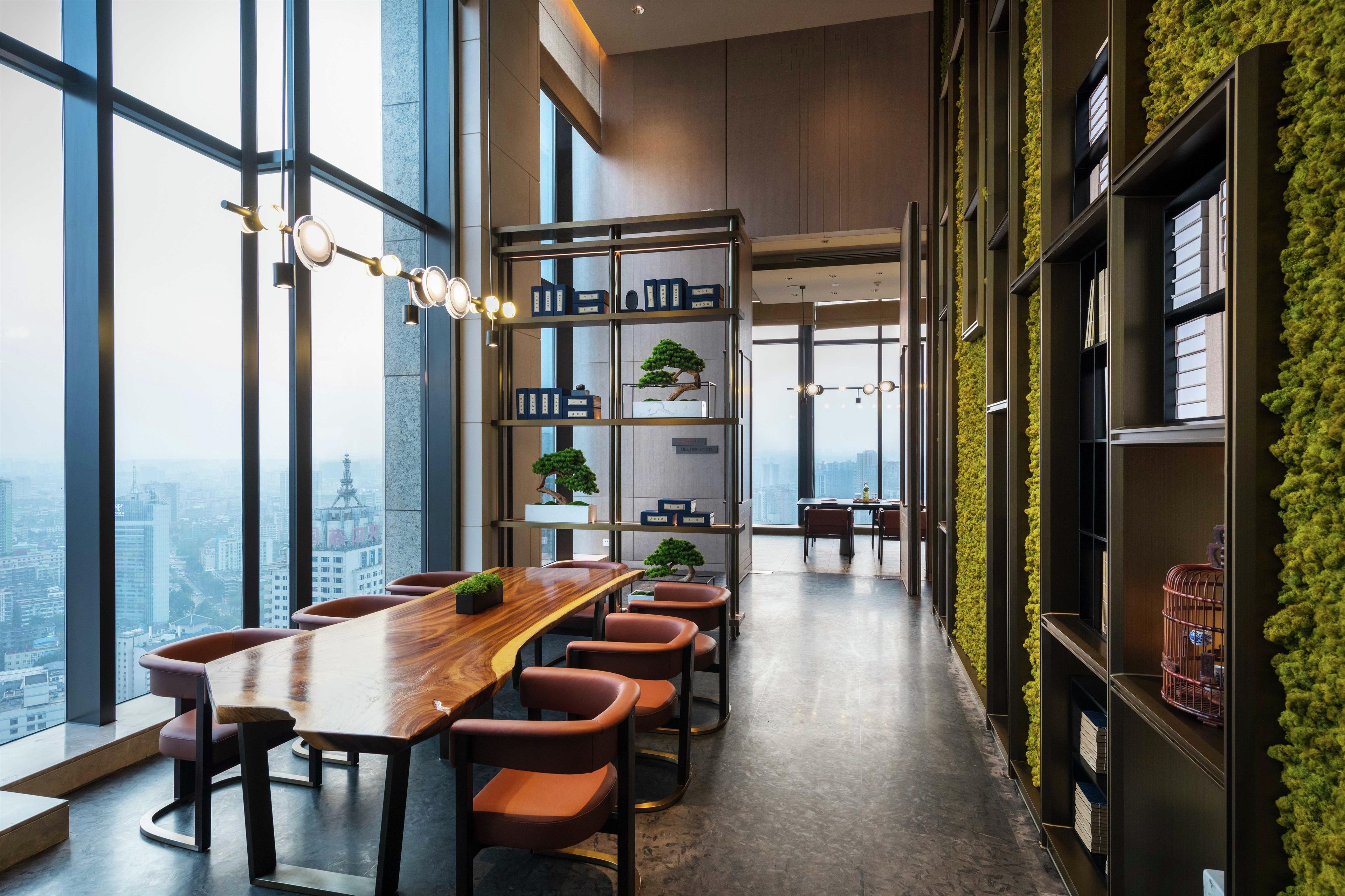 A modern conference room with a long wooden table, multiple chairs, and a bookshelf with plants.