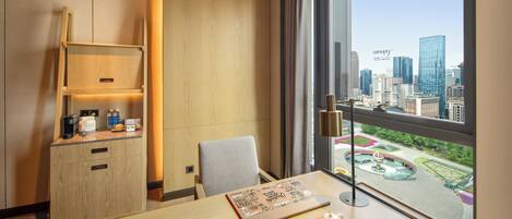A hotel room with a city view, a desk with a laptop, a chair, a wooden cabinet, and a window with curtains.