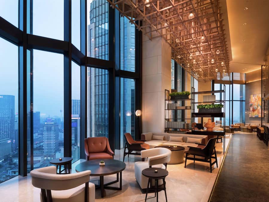 Un vestíbulo amplio con techos altos, ventanas grandes que ofrecen vistas a la ciudad, mobiliario moderno y un diseño de techo único.