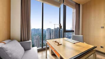 Una habitación de hotel moderna con un ventanal grande, un sofá, un escritorio de madera y vistas a la ciudad.