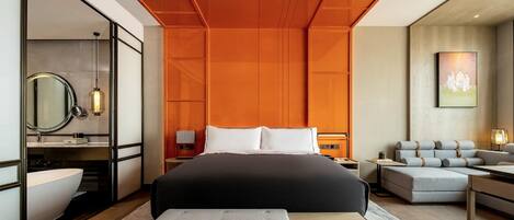 A modern hotel room with a large bed, a bedside table, a bench, a sofa, a desk, and a painting on the wall.