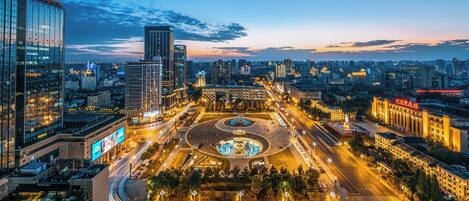 A cityscape with modern buildings, a roundabout, and a large open plaza with a fountain.