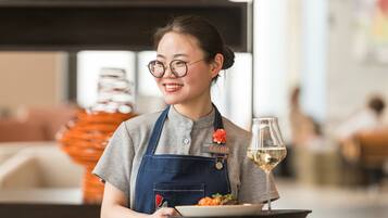 A person in a uniform holding a tray with a plate of food and a glass of white wine.