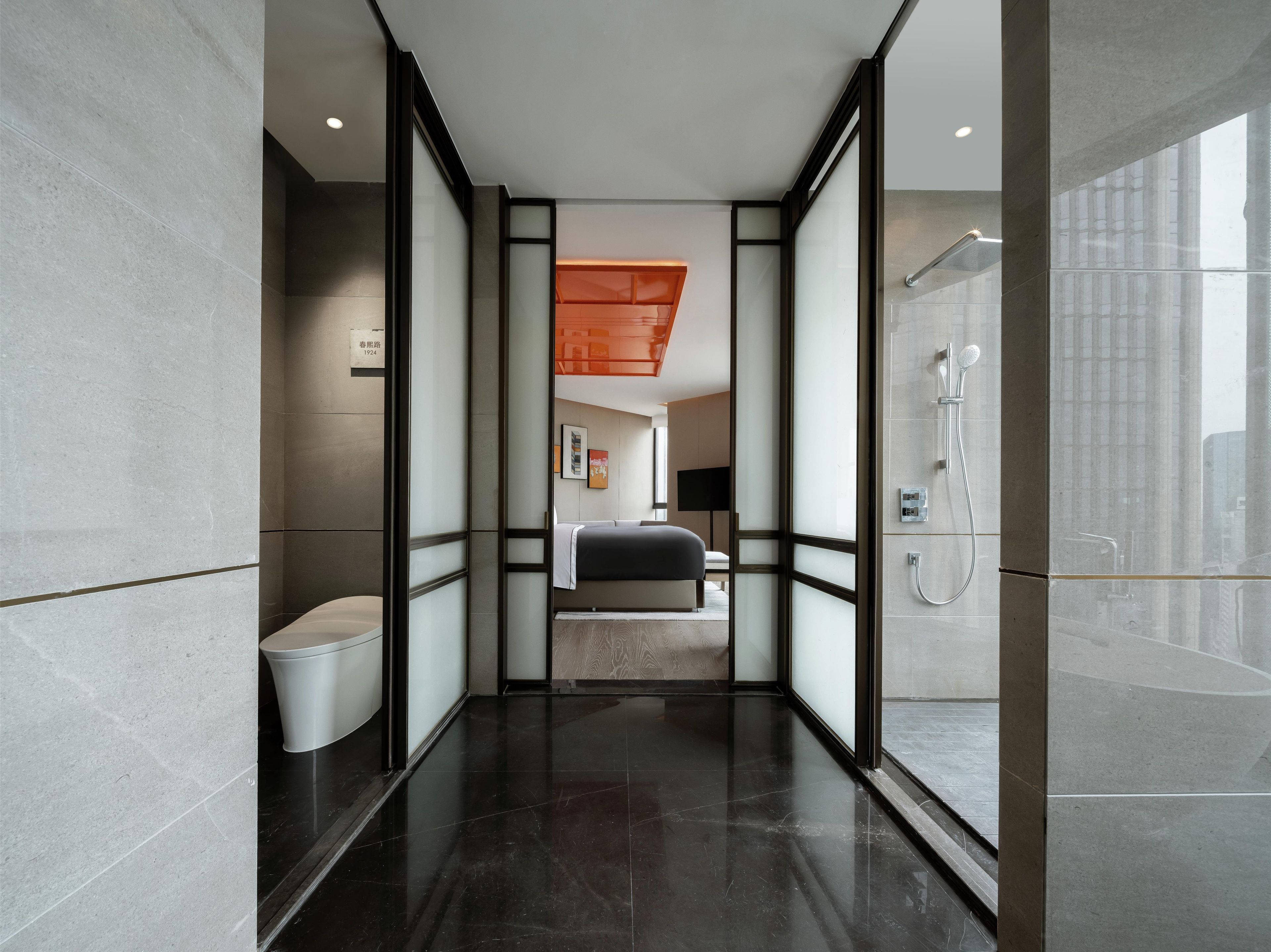 A modern bathroom with a shower, toilet, and a bed in the background.
